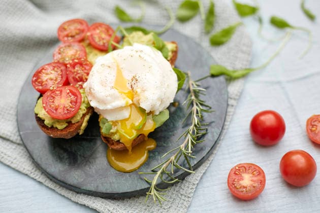 Poached egg and avocado toast with cherry tomatoes A delicious and nutritious breakfast featuring toasted bread topped with avocado, poached egg, and fresh cherry tomato slices, garnished with rosemary sprigs. Model Released LauraLibran_ID32974_1122900_021 Copyright: xLauraxLibranx RECORD DATE NOT STATED