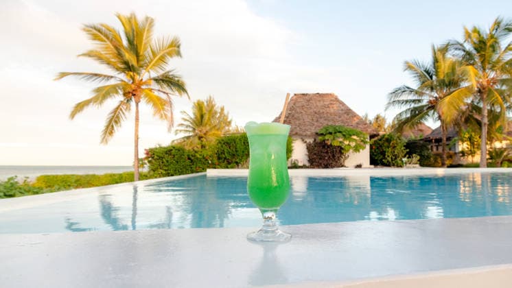 Honeymoon paradise at a Zanzibar resort pool A refreshing green cocktail by the pool at a luxurious Zanzibar resort. The serene background includes palm trees and a thatched villa, reflecting paradise. Model Released SilviaRedondo_ID33141_1127805_024 Copyright: xSilviaxRedondox RECORD DATE NOT STATED