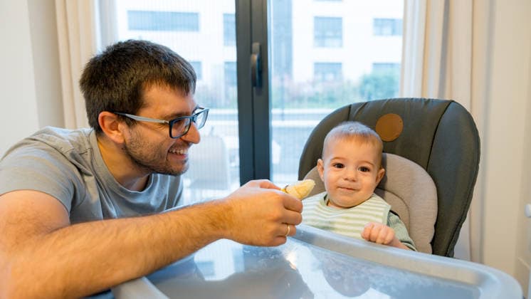 Father sharing banana with baby during mealtime A father joyfully shares a banana with his baby during a mealtime in the kitchen. The baby, seated in a high chair, seems curious and excited about trying new foods. Model Released SilviaRedondo_ID33605_1170090_006 Copyright: xSilviaxRedondox RECORD DATE NOT STATED
