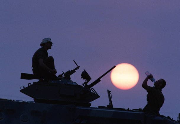 February 23, 1991, Qatar: Canadian Forces Pt. Dominque Benoit takes a drink of water while Cpl. Robert St. Laurent watches on Feb. 23, 1991, during a break while on patrol with their Grizzly armoured patrol carrier in Qatar during the Gulf War. The sun sets in a hazy sky as fires burn in Kuwait. (CP PHOTO ) Qatar  - ZUMAc35_ 19910223_zaf_c35_002 Copyright: xHansxDerykx
