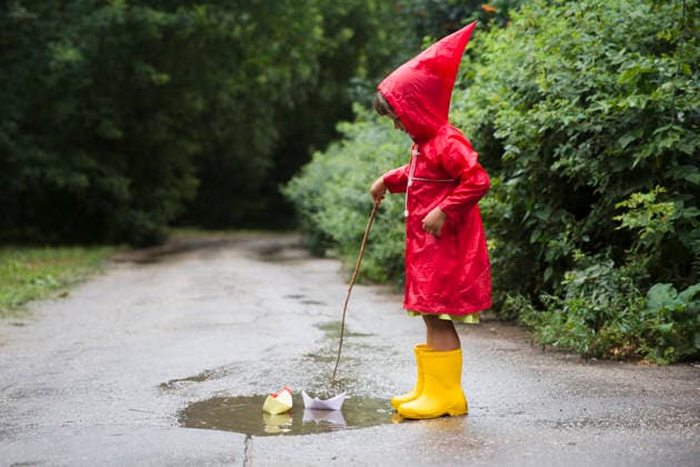 Ein Kind in einem roten Regenmantel und gelben Gummistiefeln spielt nach einem Sommerregen mit Papierbooten in einer Pfütze. a child in red raincoat and yellow rubber boots playing with paper boats in a puddle after rain in the summer (License=RF) ,model released, Symbolfoto Copyright: xZoonar.com UliaxZotaninax 24710694 ,model released, Symbolfoto ,property released