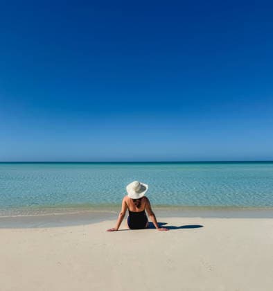 Woman in swimsuit sunhat sitting on tropical beach looking at ocean. Grace Bay, Caicos Islands, Turks and Caicos Islands CR_DOHO26022882-1973352-01 ,model released, Symbolfoto