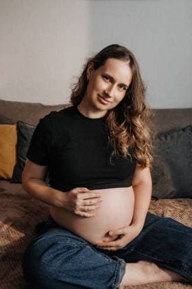 Smiling pregnant woman touching her belly while sitting. Vladivostok, Primorsky Krai, Russia R_SDXK260225-1974254-01 ,model released, Symbolfoto