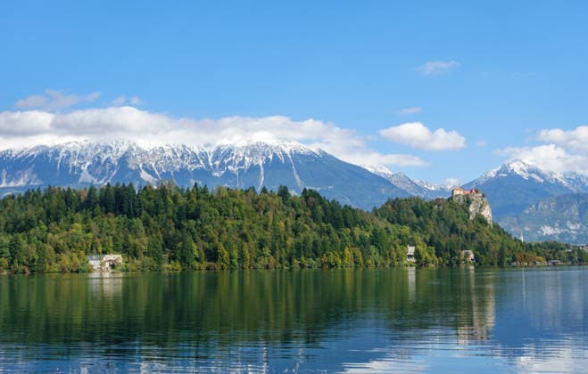 Panoramablick auf den Bleder See mit seiner ikonischen Burg auf einer Klippe und schneebedeckten Alpengipfeln. Ein Symbol für Naturschutz, alpine Biodiversität und nachhaltigen Tourismus in einer unberührten Umgebung *** Panoramic view at the Bleder Lake with its iconic Burg at a Cliff and snow-covered Alpine peaks a symbol for Nature conservation, Alpine Biodiversity and sustainable Tourism in a untouched Environment 1135900203