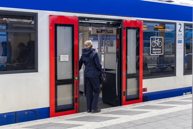 Augsburg, Bavaria, Germany - March 4, 2026: A train attendant stands at an open door in front of a regional train on the platform. Train staff check tickets, assist passengers, and ensure order and safety during local train journeys. *** Eine Zugbegleiterin des Bahnverkehrs steht an einer geöffneten Tür vor einem Regionalzug am Bahnsteig ein. Zugpersonal kontrolliert Tickets, unterstützt Fahrgäste und sorgt für Ordnung und Sicherheit während der Zugfahrt im Nahverkehr.