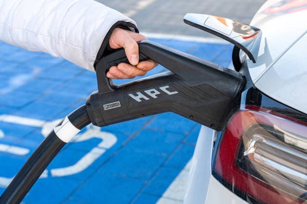 Eine Hand verbindet ein Elektroauto mit einem Schnellladestecker. Die Aufnahme zeigt die einfache Handhabung moderner Ladetechnik im Alltag für eine klimafreundliche Mobilität.