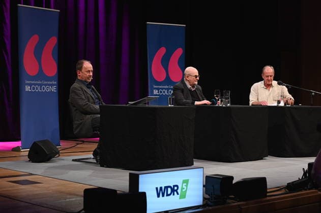 Schauspieler Ulrich Noethen, l-r, Autor Salman Rushdie und Moderator Bernhard Robben liest und spricht auf der Lit.Cologne, dem internationalen Literaturfestival