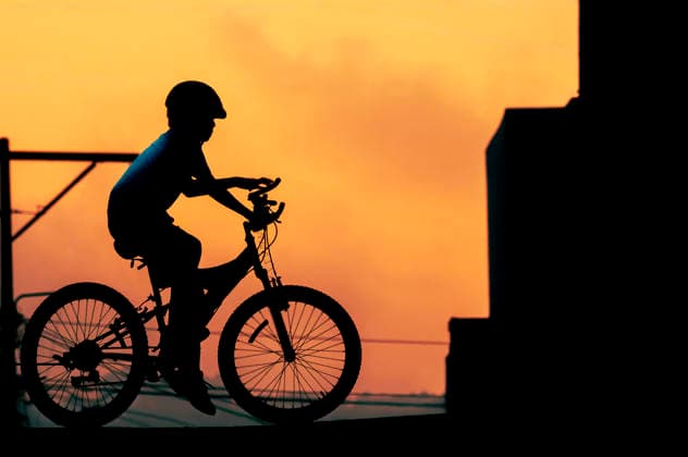 Silhouette of young boy riding bicycle at sunset with urban skyline Guatemala City, Guatemala Department, Guatemala R_BYBY260318-1986327-01