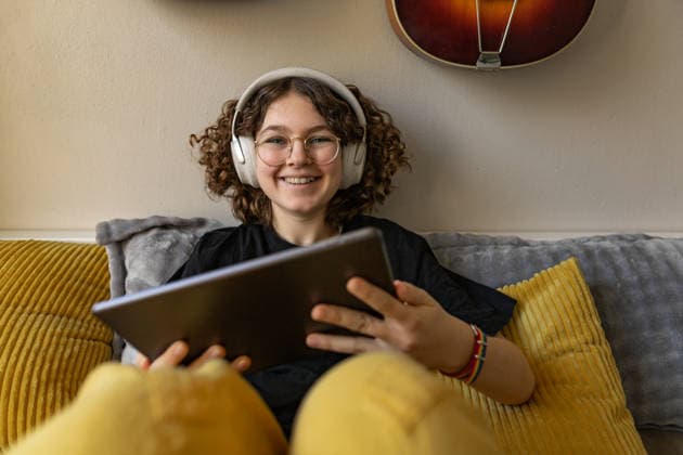 Smiling youth relaxing with headphones and tablet in cozy bedroom model released, Symbolfoto property released, Mainz RLP Germany ALPF00071