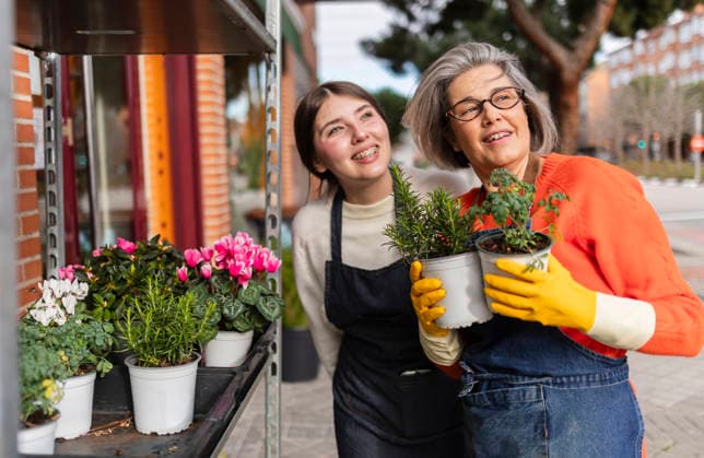 Florist assisting apprengtice with potted flowers outdoors smiling model released, Symbolfoto property released, JCCMF14566