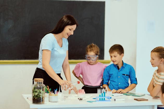 Eine Lehrerin leitet ein praktisches naturwissenschaftliches Experiment mit Schülern in einem hellen Klassenzimmer A smiling teacher guides a small group of elementary students through a hands-on science experiment, with safety goggles, test tubes and active participation fostering curiosity, learning and teamwork. (License=RF) ,model released, Symbolfoto Copyright: xZoonar.com BENISxARAPOVICx 24814885 ,model released, Symbolfoto ,property released