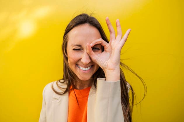 Smiling woman making ok gesture in front of yellow background model released, Symbolfoto, JCCMF14755