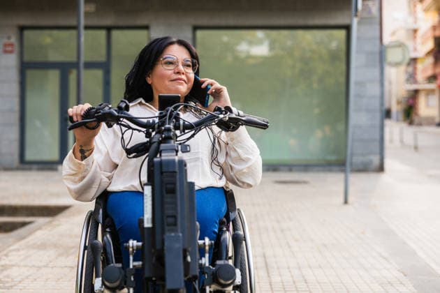 Woman using wheelchair handbike and smartphone in urban street model released, Symbolfoto property released, JMIF00062