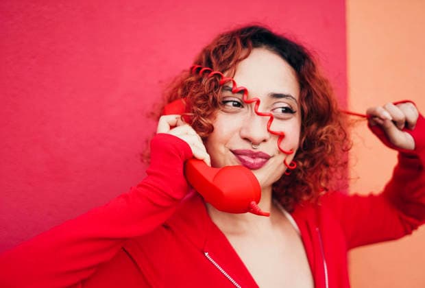 Redhead with curly hair playfully talking on red telephone indoors model released, Symbolfoto, SVCF00604