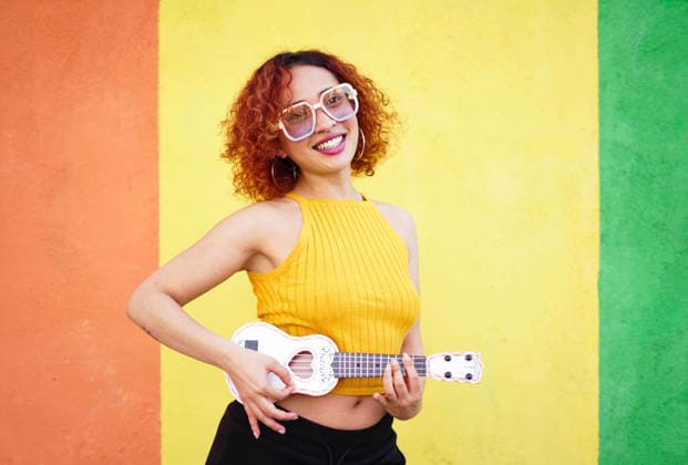 Smiling redhead with glasses playing ukulele in front of colorful wall model released, Symbolfoto, SVCF00622