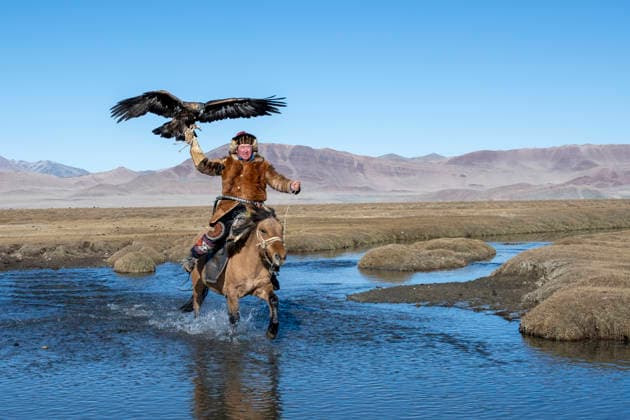 Traditional eagle hunter on horseback crossing water in Altai Mountains model released, Symbolfoto, TOVF00437
