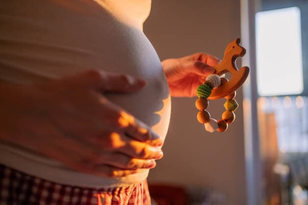 Eine schwangere Frau, die sanft ihren Bauch streichelt, während sie ein Beißspielzeug aus Naturholz und Silikon in der Hand hält ? ein Symbol für die Vorfreude und die Freude auf ein neues Leben während der Schwangerschaft Expectant mother softly resting her hand on her belly as she cradles a teething toy made of natural wood and silicone, symbolizing the happiness and anticipation of new life during pregnancy (License=RF) ,model released, Symbolfoto Copyright: xZoonar.com ElenaxShishkinax 24819959 ,model released, Symbolfoto ,property released
