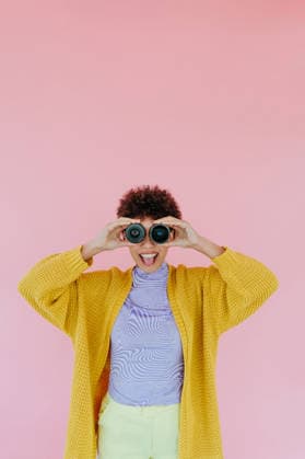 Smiling woman with binoculars wearing yellow sweater on pink background model released, Symbolfoto property released, YTF04643