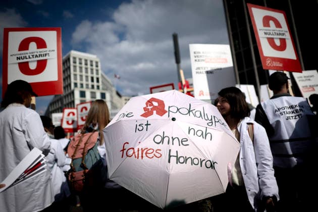 Apotheken-Protesttag DEU, Deutschland, Germany, Berlin, 23.03.2026 Demonstranten und Apotheker mit Schirm Die Apokalypse ist nah ohne faires Honorar waehrend des Protestzug im Rahmen von einem Protesttag von Apotheken unter dem Motto Apotheken gibt es nicht zum Nulltarif in Berlin Deutschland . Bundesweit wird mit Demonstrationen und einer eintaegigen Schließung der Apotheken protestiert. Protest der Bundesvereinigung Deutscher Apothekerverbände ABDA gegen steigende Kosten Lieferengpaesse und eine unzureichende Verguetung. Der Apothekerverband beklagt ein Apothekensterben und beklagt dass gesetzliche Zuschüsse auf rezeptpflichtige Medikamente seit 13 Jahren nicht mehr erhoeht wurden. en: Demonstrators and pharmacists with umbrellas:The a