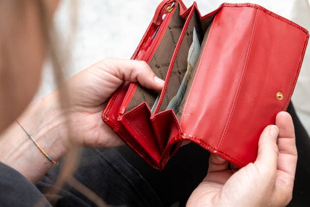 Eine Frau blickt in ihre fast leere Geldbörse und steht als Symbolbild für steigende Lebenshaltungskosten, Inflation und finanzielle Sorgen im Alltag