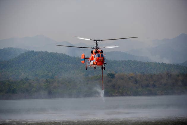 March 27, 2026, Chiang Mai, Thailand: A helicopter performs water pickup operations over a reservoir in Chiang Mai, northern Thailand, as part of aerial firefighting efforts against ongoing wildfires. A KA-32 helicopter from the Department of Disaster Prevention and Mitigation skims the water surface to collect water before heading to fire-affected forest areas amid hazy conditions caused by smoke and rising PM2.5 pollution. Chiang Mai Thailand - ZUMAs197 20260327_aaa_s197_321 Copyright: xPongmanatxTasirix