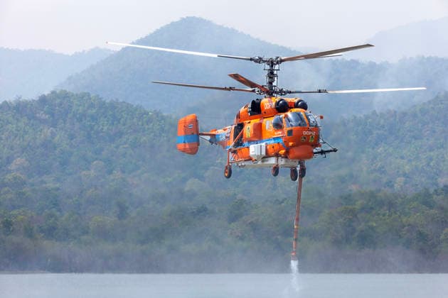 March 27, 2026, Chiang Mai, Thailand: A helicopter performs water pickup operations over a reservoir in Chiang Mai, northern Thailand, as part of aerial firefighting efforts against ongoing wildfires. A KA-32 helicopter from the Department of Disaster Prevention and Mitigation skims the water surface to collect water before heading to fire-affected forest areas amid hazy conditions caused by smoke and rising PM2.5 pollution. Chiang Mai Thailand - ZUMAs197 20260327_aaa_s197_342 Copyright: xPongmanatxTasirix