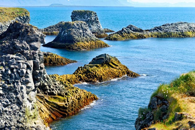 Creative Highlights World Die Klippen von Arnarstapi zeigen die felsige Küste Islands Rocky formations rise from the water near Arnarstapi in Iceland. The clear blue water surrounds these natural structures under bright sunlight. (License=RF) Copyright: xZoonar.com MarcoxBriviox 24844833