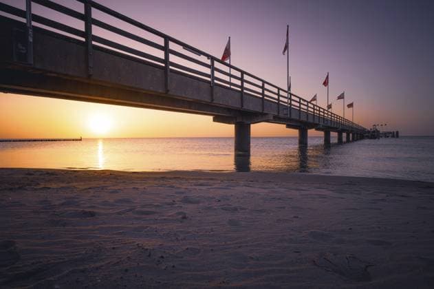 Ein Pier im Licht eines Sonnenaufganges über dem ruhigen Meer mit violettem Himmel, der Blick über den Sandstrand entlang der Seebrücke auf die Ostsee, Südstrand in 23775 Großenbrode, Deutschland A pier in the light of sunrise over the calm sea with purple sky, the view across the sandy beach along the pier to the Baltic Sea, Südstrand in 23775 Großenbrode, Germany Copyright: imageBROKER FrankxNiehaus ibxfni17195542.jpg