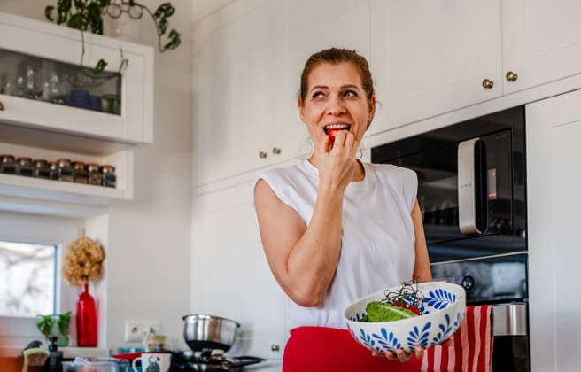 Woman tasting fresh salad while cooking healthy meal. Woman tasting fresh salad while cooking healthy meal at home. model released