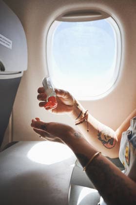 Hands, flight and woman in airplane with sanitizer, travel and tourism for passenger in aircraft. Vacation, disinfection and safety for person with holiday, trip and window for health compliance. model released property released Copyright: xROWANxJORDAN(PTY)LTDx
