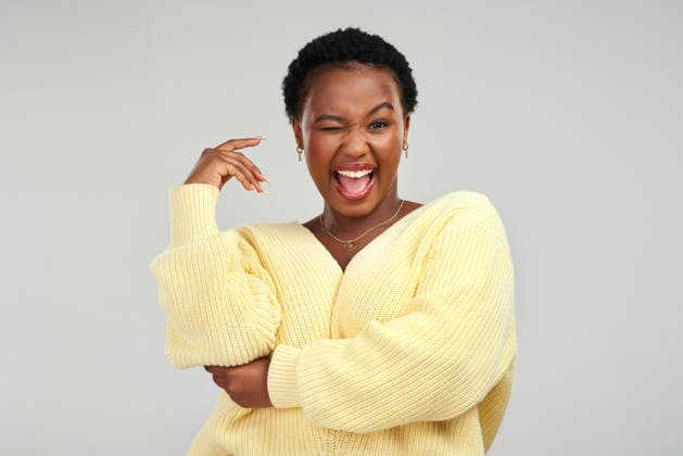 Portrait, black woman and wink in studio, excited and funny expression on white background. Smile, person and blink for flirt, playful sign and laughing with eye emoji for secret gesture in Kenya. model released property released Copyright: xwww.peopleimages.comx