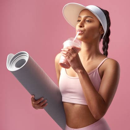 Fitness, smoothie and woman in studio with yoga mat, mineral balance and nutrition for post exercise detox. Drink, pilates equipment and person with shake for weight loss, vitamins or pink background. model released property released Copyright: xwww.peopleimages.comx