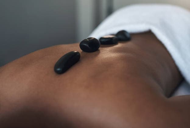 Client, back and hot stone massage in spa, muscle relaxation therapy and holistic body care treatment. Warm rocks, skincare detox and person with stress relief for healing, wellness retreat and rest. model released property released Copyright: xwww.peopleimages.comx