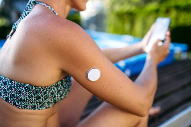 Diabetic woman with CGM on arm checking her blood sugar, sitting by pool. Diabetic woman with CGM on arm checking her glucose level on phone, sitting by pool. model released