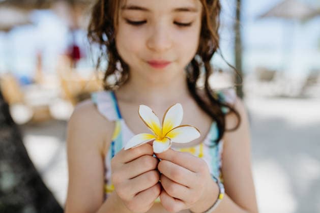 Happy child smelling tropical flower during family vacation at beach resort. Happy child smelling tropical flower during family vacation at beach resort. Summer holiday. model released