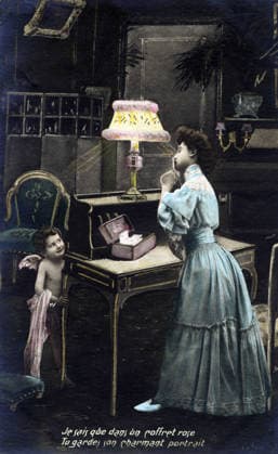 Secret of Love: A young woman signals to a little Cupid hiding behind a desk not to reveal her secret. She keeps a portrait of her lover in a box. Postcard from the early 20th century RECORD DATE NOT STATED