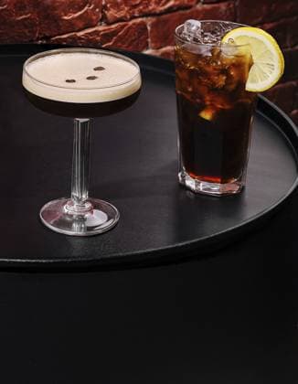 IMAGO Creative, Food, Trend, Iced Coffee Food, Zwei Cocktails werden auf einem schwarzen runden Tisch präsentiert. Eines ist ein cremefarbenes Getränk, garniert mit Kaffeebohnen, und das andere ist ein dunkles Eisgetränk mit einer Zitronenscheibe Food, Two cocktails are presented on a black round table. One is a smooth cream-colored drink garnished with coffee beans, and the other is a dark iced beverage with a lemon slice Copyright: imageBROKER AntonxDobrea ibxiqx17124215.jpg