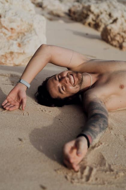 Tattooed man lying on sand smiling at camera with arm outstretched Kuta Selatan, Bali, Indonesia CR_YUKI260413AF-1993131-01 ,model released, Symbolfoto