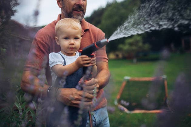 Little daughter helping dad in garden, watering plants with hose. Little daughter helping dad in garden, watering plants with garden hose. model released