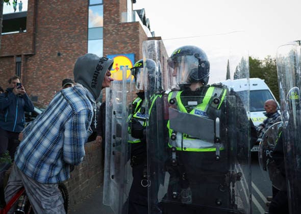 April 20, 2026, Epsom, Surrey, UK: Epsom, UK. A protester taunts police in riot gear as a large crowd gathers in Epsom, Surrey, asking for transparency and accountability from the police regarding a recent alleged gang rape in the town. Epsom UK  - ZUMAl94_ 20260420_zaf_l94_096 Copyright: xJacquelinexLawriex