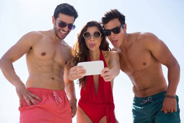 Low angle view of young friends taking selfie against clear sky Low angle view of young friends taking selfie through mobile phone against clear sky at beach, model released, Cape Town, South Africa, 17.01.2017, 979470.jpg, friend, friendship, selfie, mobile phone, clear sky, beach, happy, sunglasses, sunny, holding, making a face, sticking out tongue, standing, side by side, sunlight, shirtless, shorts, together, bonding, enjoyment, fun, happiness, vacation, weekend activities, lifestyle, leisure, summertime, bright, beachwear, bikini, protection, safety, swimsuit, swimwear, red, hand on hip, connection, wireless, cellphone, smartphone, wireless technology, photographing, photography themes Outdoors,Front view,Low angle view,Focus on For