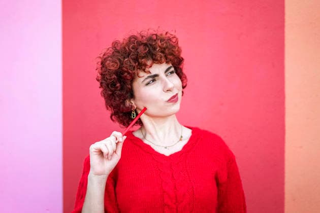 Curly redhead in red sweater thinking with pencil against vibrant background model released, Symbolfoto, SVCF00662