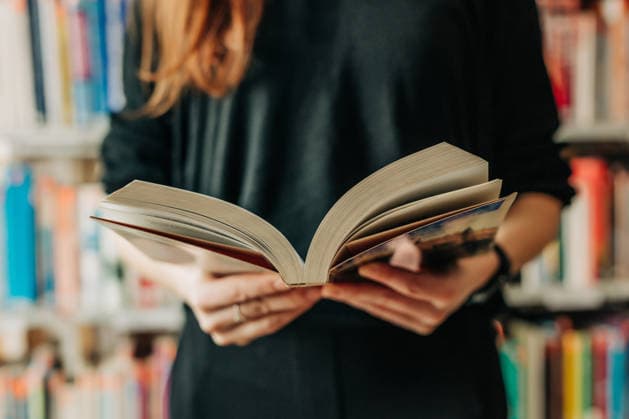 Unrecognizable person holding an open book in a library model released, Symbolfoto, VSNF04782