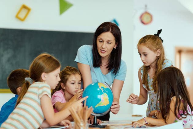 Ein Lehrer zeigt einem Globus neugierigen Grundschülern, die sich um einen Tisch in einem hellen Klassenzimmer versammelt haben A teacher guides a small group of elementary students as they explore a globe together, encouraging curiosity, geography learning and collaborative engagement during a hands-on classroom lesson. (License=RF) ,model released, Symbolfoto Copyright: xZoonar.com BENISxARAPOVICx 24925959 ,model released, Symbolfoto ,property released