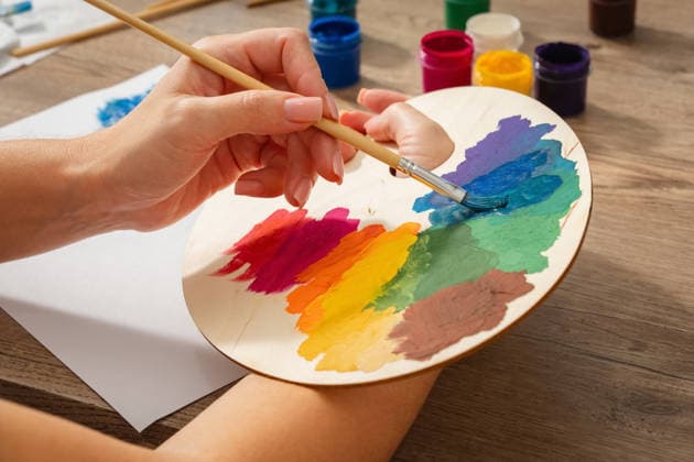 Ein linkshändiges Mädchen trägt mit einem Pinsel blaue Farbe auf eine Holzpalette auf. Das Bild ist voller leuchtender Farben und erinnert an einen Regenbogen. Ihr Hobby ist das Zeichnen. A left-handed girl is using a brush to apply blue paint to a wooden palette. The painting is full of vibrant colors and resembles a rainbow. Her hobby is drawing. (License=RF) Copyright: xZoonar.com AndreyxMaksimovx 24934326