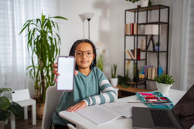 Junger Schüler, der sein Smartphone mit leerem Bildschirm für den Online-Unterricht zeigt Young girl holding a smartphone with a white screen, sitting at a desk and studying (License=RF) ,model released, Symbolfoto Copyright: xZoonar.com JelenaxCvetkovicx 24950612 ,model released, Symbolfoto ,property released