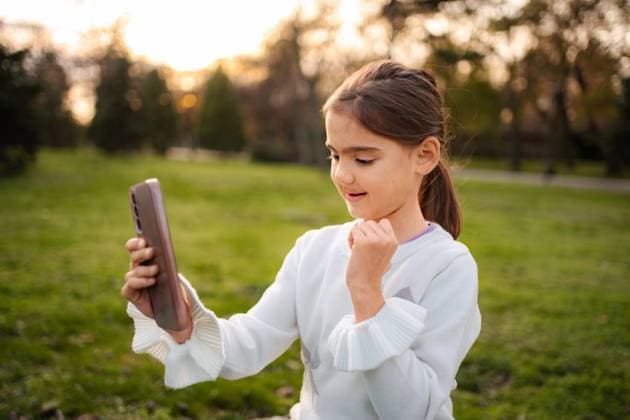 Ein junges Mädchen führt im Park ein Videogespräch mit Freunden und Familie Girl smiling making video call on smartphone outdoors, connecting with family and friends (License=RF) ,model released, Symbolfoto Copyright: xZoonar.com JelenaxCvetkovicx 24958917 ,model released, Symbolfoto ,property released