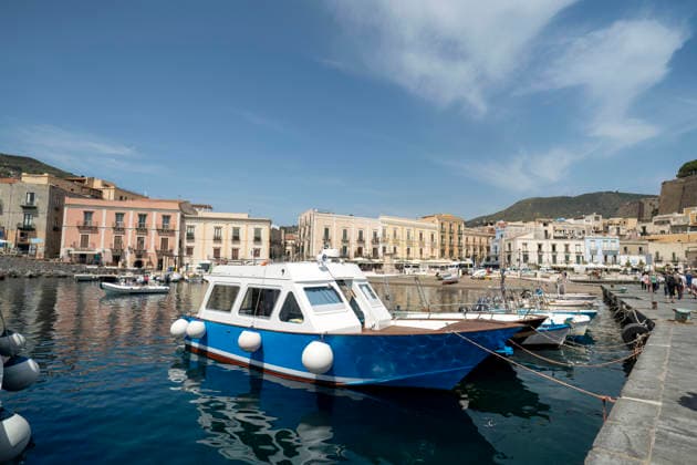 Ein traditionelles blau-weißes Fischerboot, das im Hafen von Mondello auf Sizilien vor Anker liegt. Bunte historische Gebäude säumen die Uferpromenade am Mittelmeer. Eine Szene aus einem italienischen Küstendorf. Traditional blue and white fishing boat moored in Mondello harbor, Sicily. Colorful historic buildings line the waterfront with Mediterranean Sea. Italian coastal village scene. (License=RF) Copyright: xZoonar.com ArpanxBhatiax 24973547
