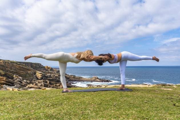Zwei Frauen praktizieren im Freien auf einer grasbewachsenen Klippe mit Blick auf den Ozean Acro Yoga und halten zusammen eine tiefe Kriegerpose ein, die Balance, Teamwork und Wohlbefinden symbolisiert Two women practicing acro yoga outdoors on a grassy cliff overlooking the ocean, holding a deep warrior pose together, symbolizing balance, teamwork, and wellness Copyright: imageBROKER UnaixHuizi ibxuhu16618149.jpg ,model released, Symbolfoto ,property released