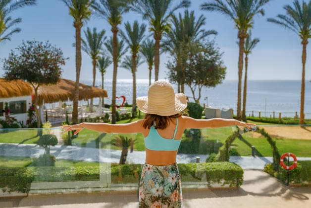 Ein kleines Mädchen mit einem Strohhut, das mit ausgestreckten Armen vom Balkon eines tropischen Ferienresorts aus auf das Meer blickt, während der Sommerferien Back view of a child enjoying the ocean view and palm trees at a luxury hotel terrace representing freedom and travel concept (License=RF) ,model released, Symbolfoto Copyright: xZoonar.com AnnaxLuryex 25021764 ,model released, Symbolfoto ,property released